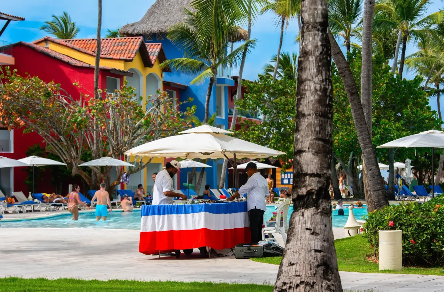 Poolside service table with staff near colorful buildings at Tropical Deluxe Princess.