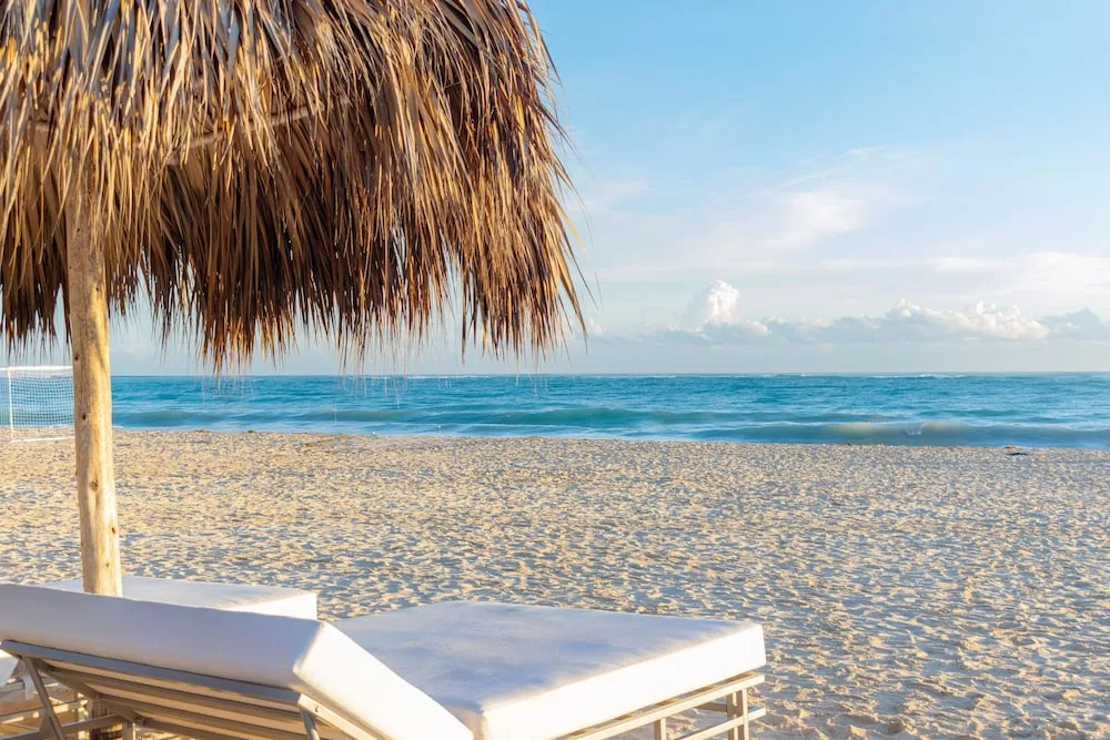 A white lounger under a thatched umbrella faces the ocean at Tropical Deluxe Princess.