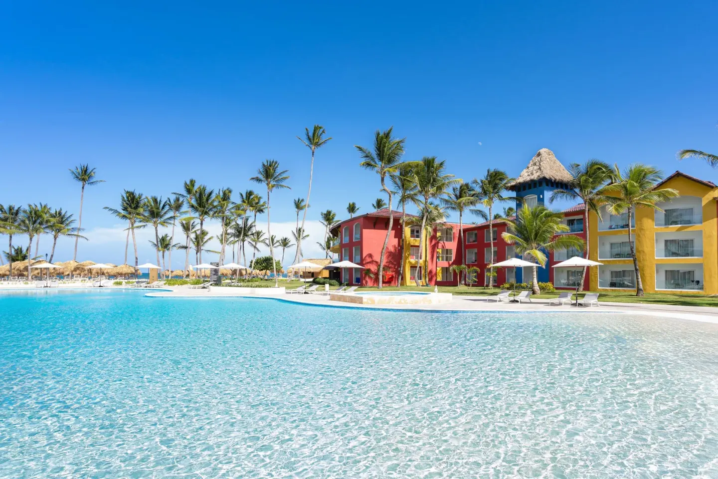 Wide turquoise pool facing colorful buildings and palm trees at Tropical Deluxe Princess.