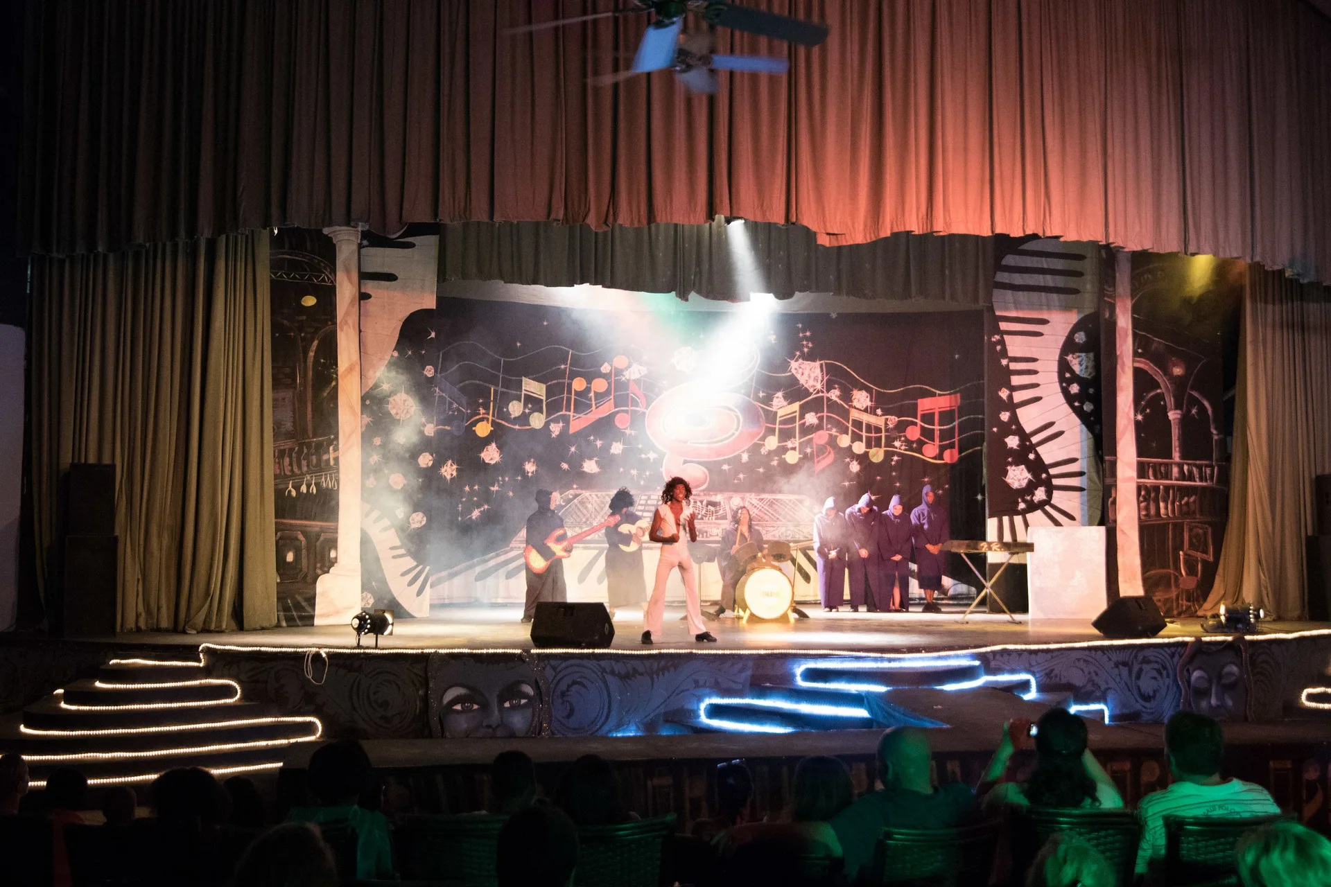 A live band performs on a lit theater stage at Tropical Deluxe Princess.