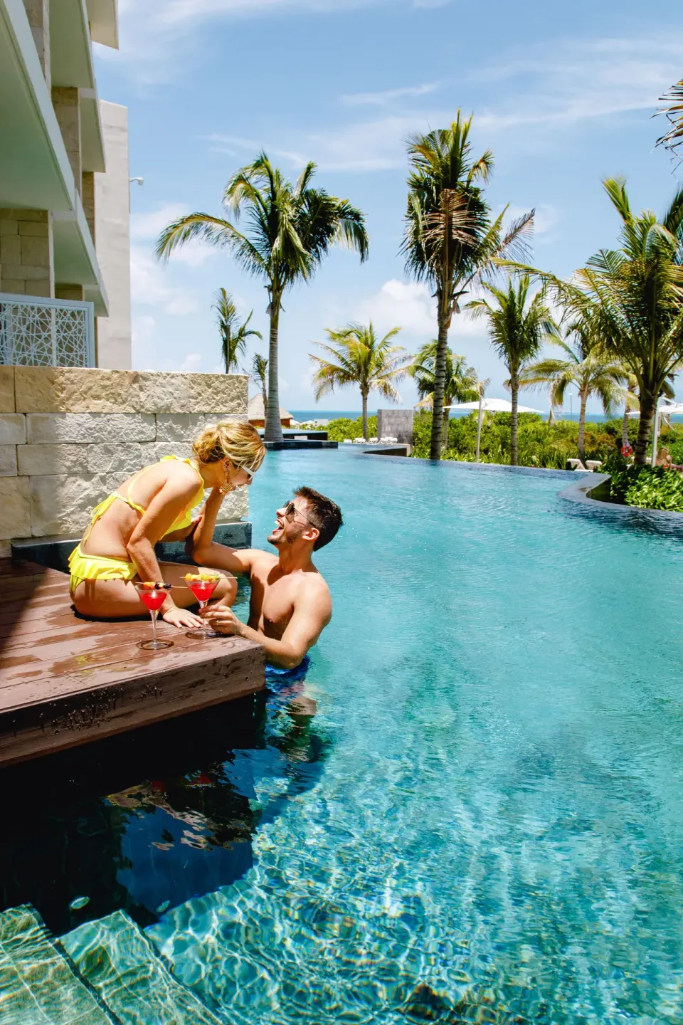 Couple with cocktails beside the pool at TRS Coral Hotel, with palms and the ocean in the distance.