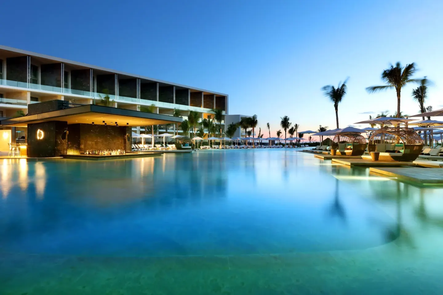Evening pool scene with glowing bar and cabana seating at TRS Coral Hotel.