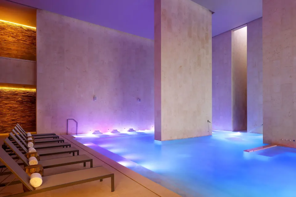Indoor spa pool with illuminated water, stone columns and loungers at TRS Coral Hotel.