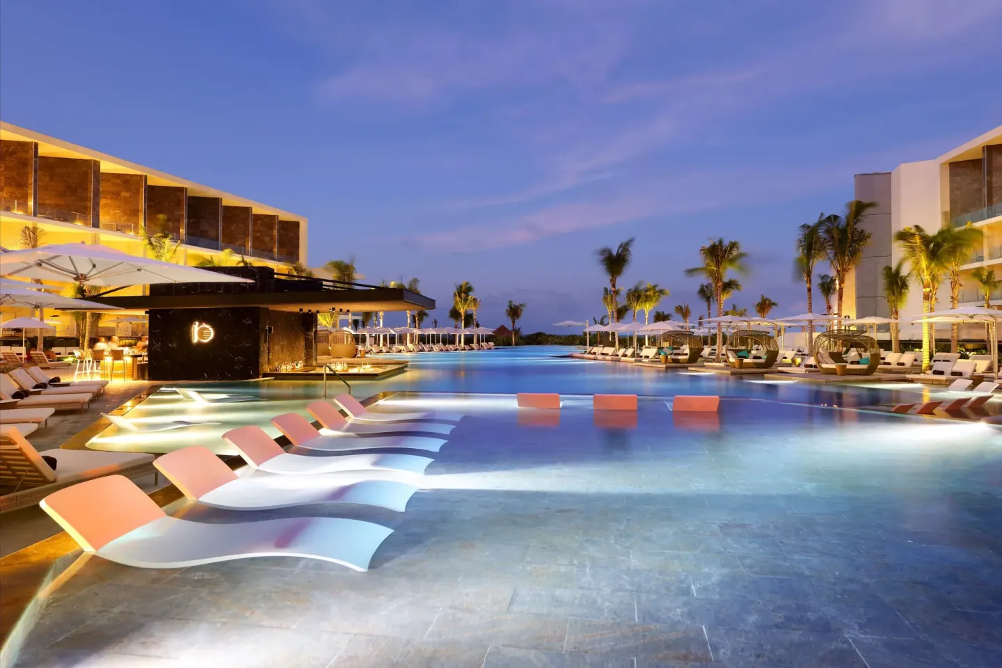 Illuminated pool with in-water loungers and cabanas at dusk at TRS Coral Hotel.