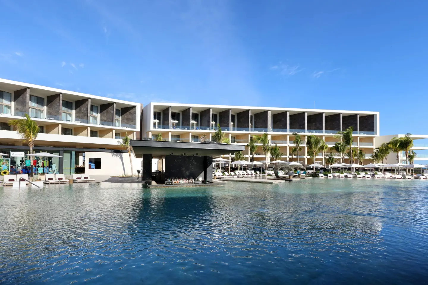 Large resort pool at TRS Coral Hotel with a swim-up bar, palm trees, loungers, and balcony buildings.