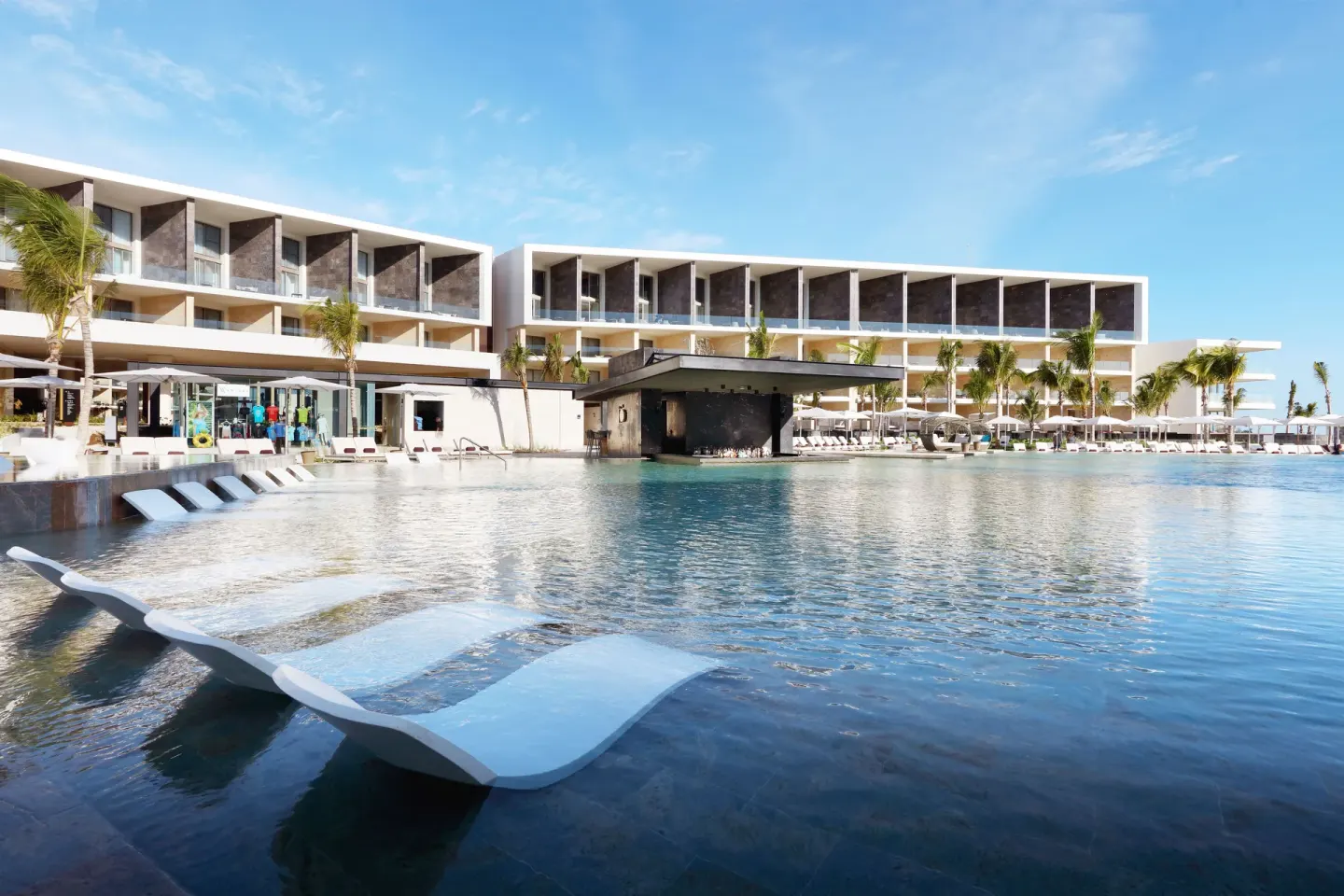 Pool and in-water chaise lounges at TRS Coral Hotel facing resort buildings and palm-lined decks.