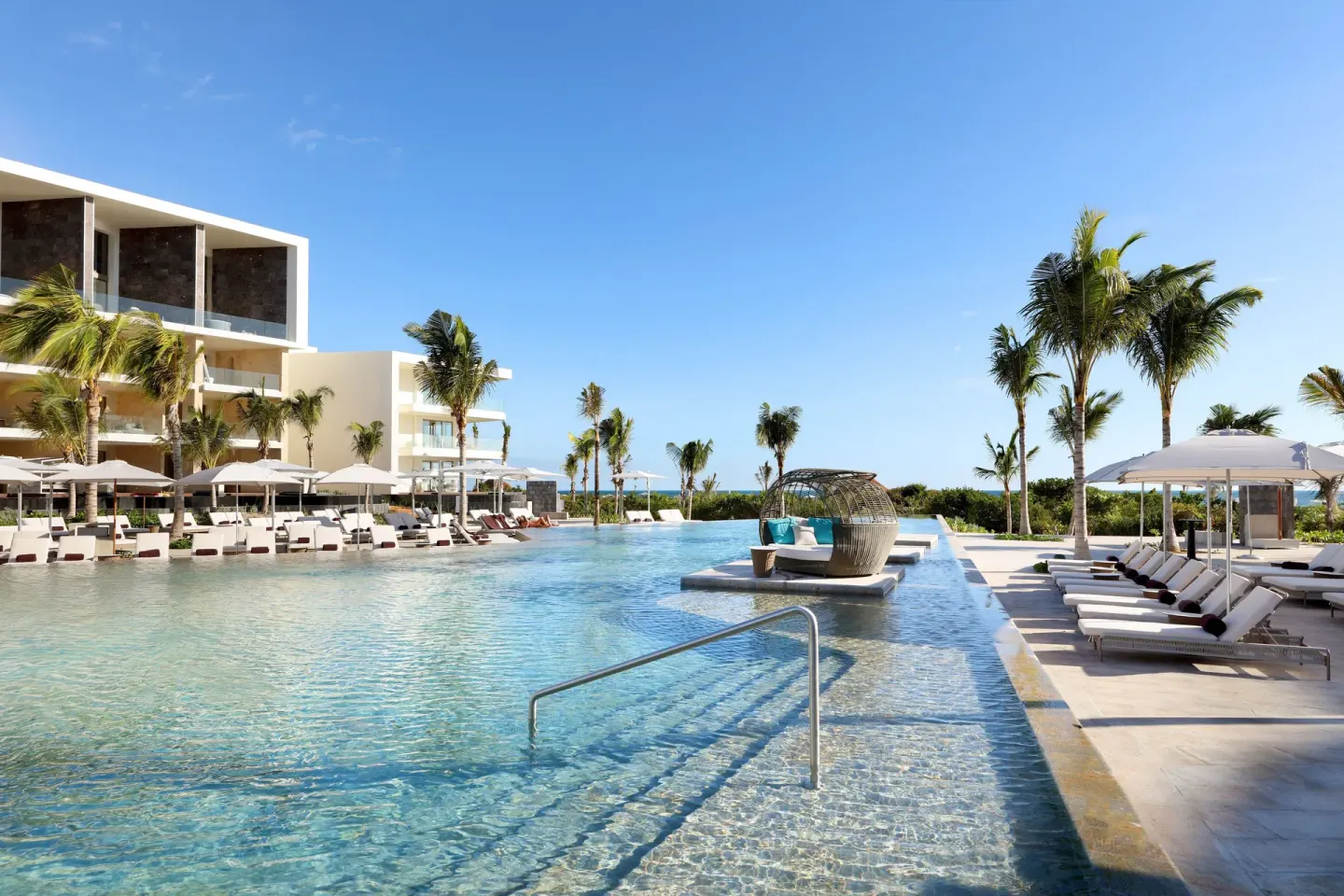 Pool steps, loungers, palms and a woven daybed beside TRS Coral Hotel.