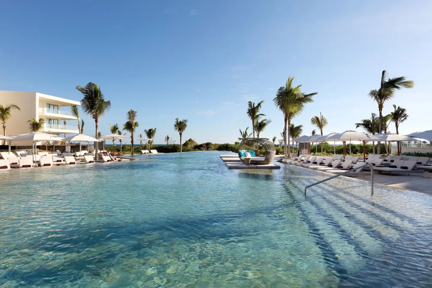 Resort pool with palm trees, umbrellas and circular daybed at TRS Coral Hotel.