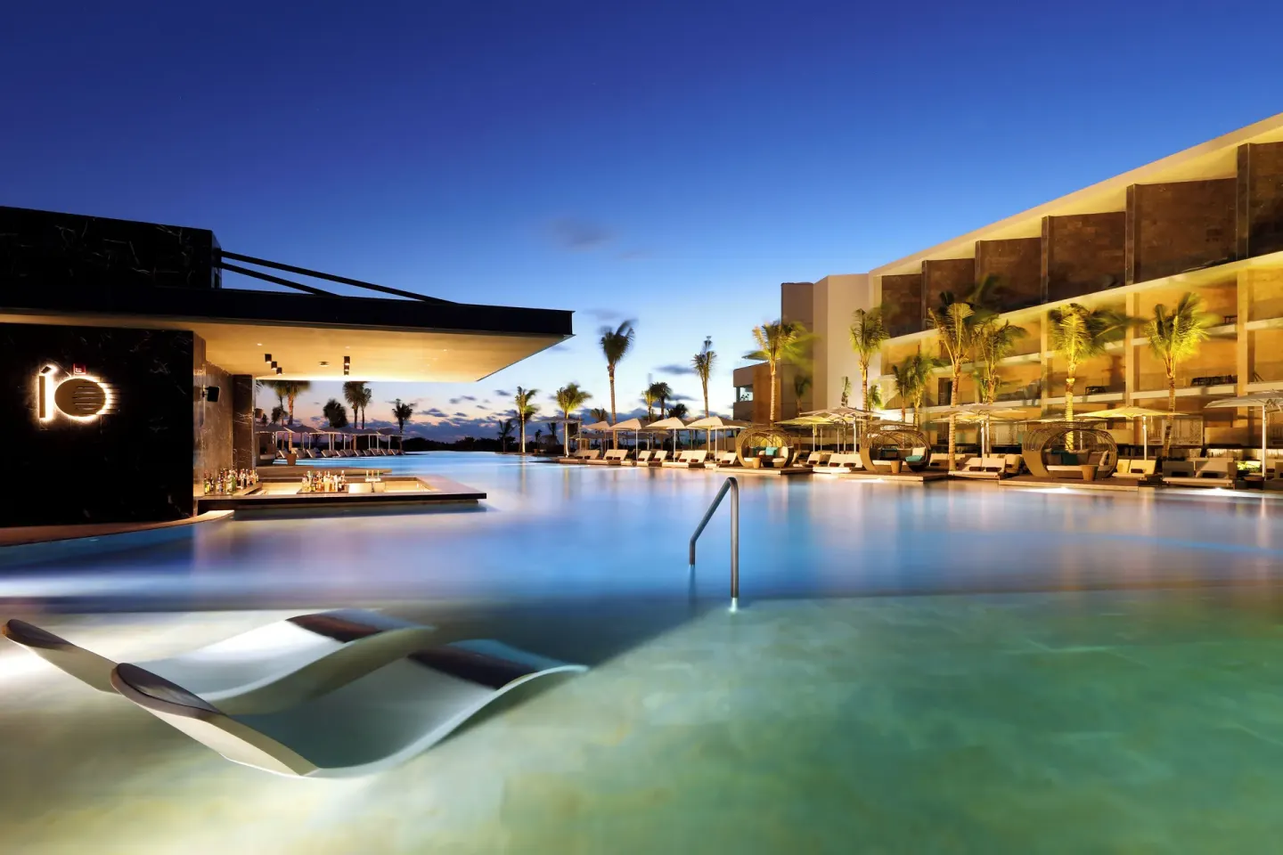 Twilight pool scene with loungers and illuminated buildings at TRS Coral Hotel.