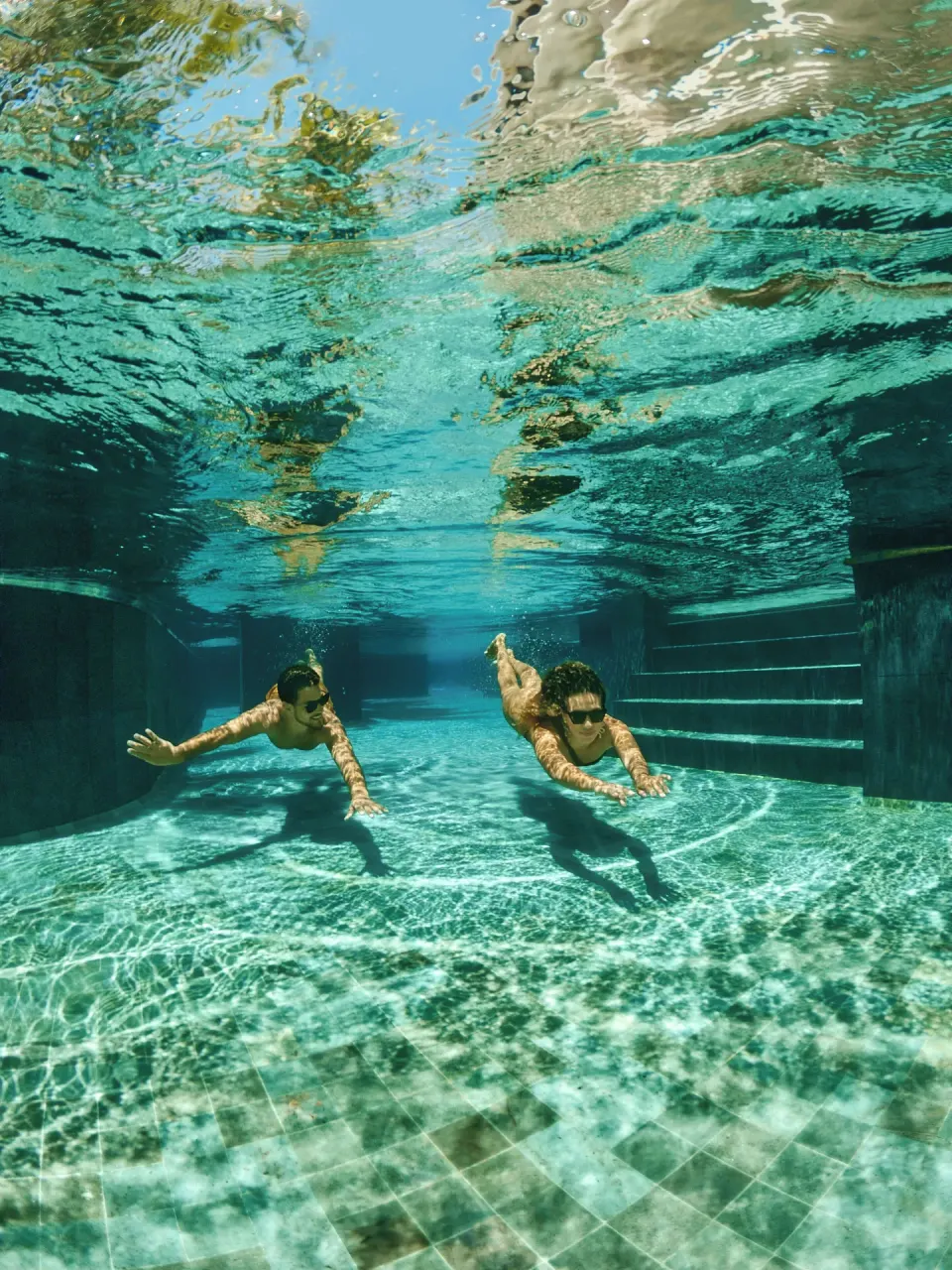 Two swimmers underwater in a tiled pool at TRS Coral Hotel.