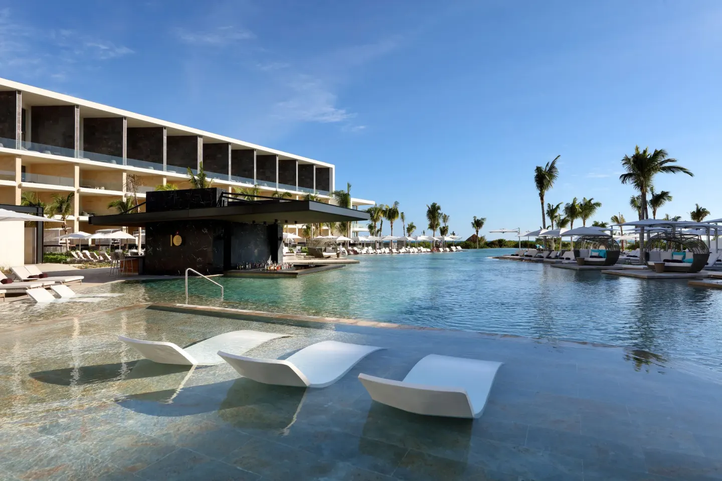 Wide pool view at TRS Coral Hotel with in-water loungers, palm trees, cabanas, and resort buildings.