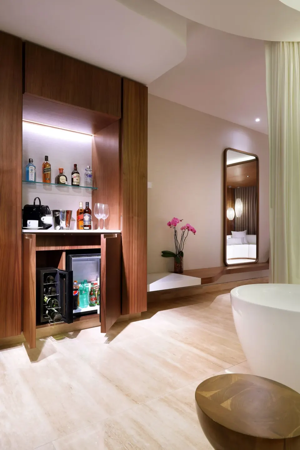 Junior Suite minibar area with open refrigerator, bottles, mirror, and tub at TRS Coral Hotel.