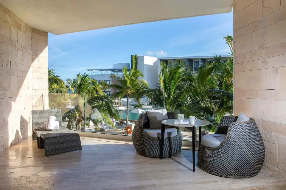 Junior Suite terrace with wicker chairs, lounger, palms, and pool glimpses at TRS Coral Hotel.