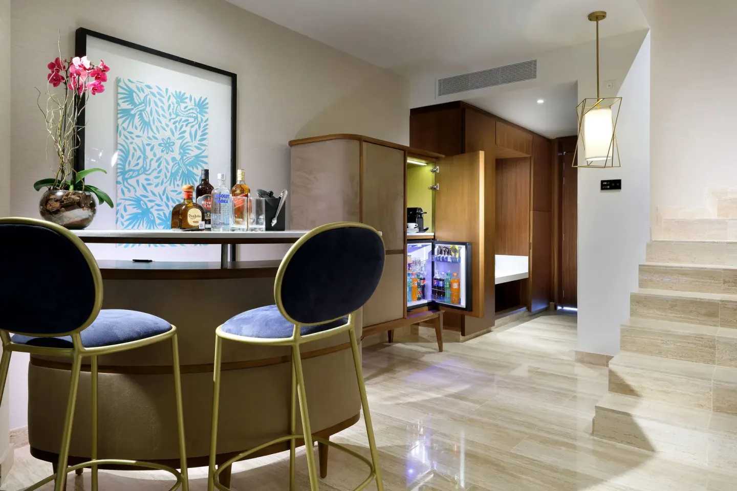 Loft Suite bar area at TRS Coral Hotel with two stools, bottles, minibar, wood cabinetry, and stairs.