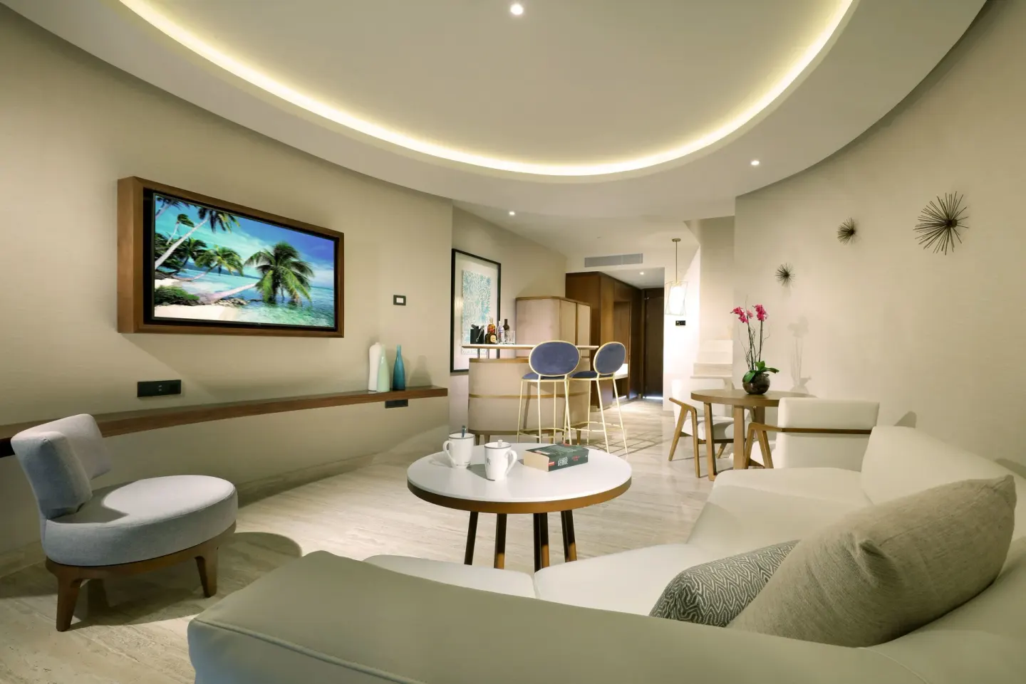 Loft Suite living room at TRS Coral Hotel with white sofa, TV, bar counter, and round ceiling light.