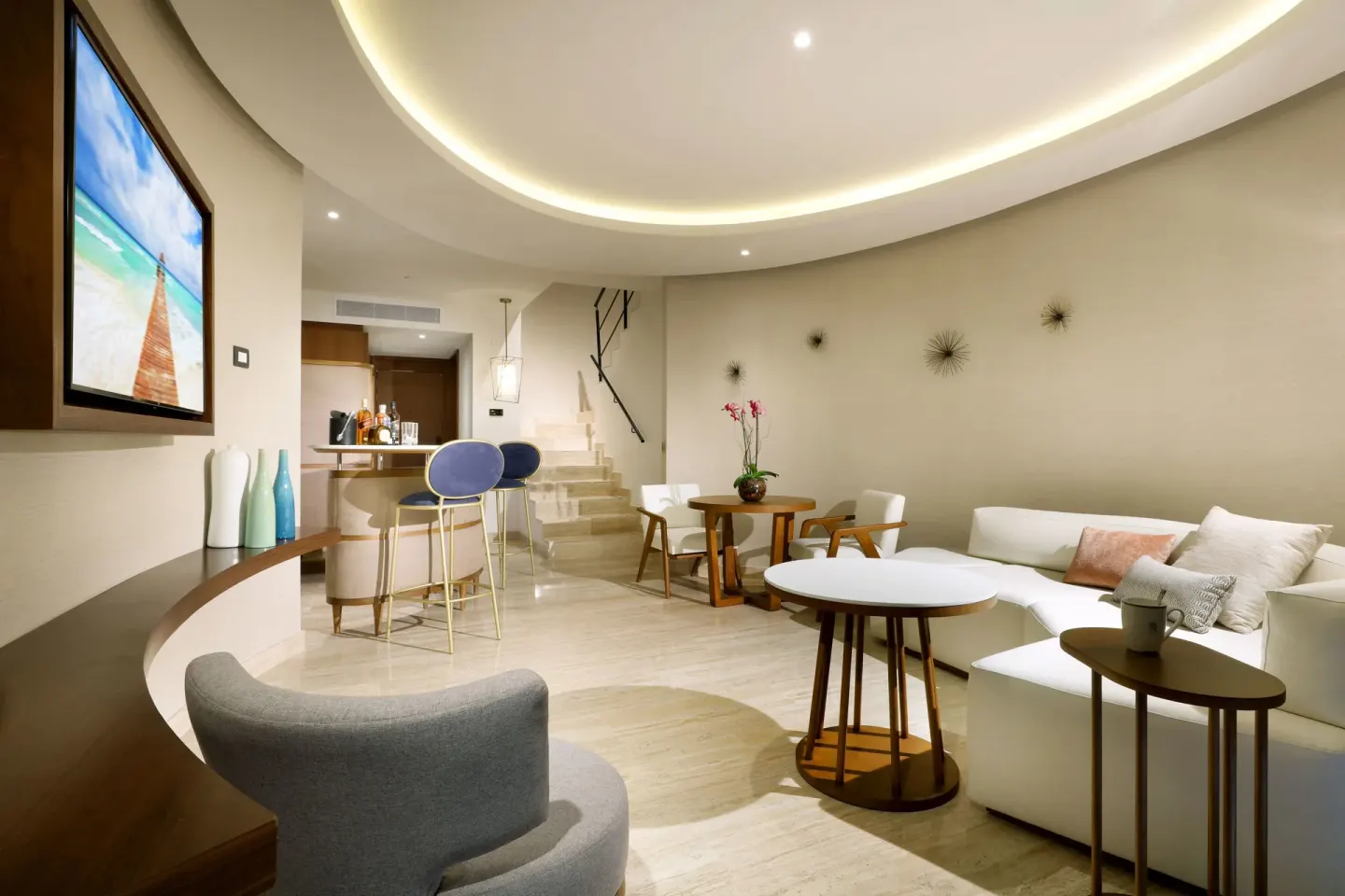 Loft Suite lounge at TRS Coral Hotel with sofa seating, TV, bar stools, and staircase.