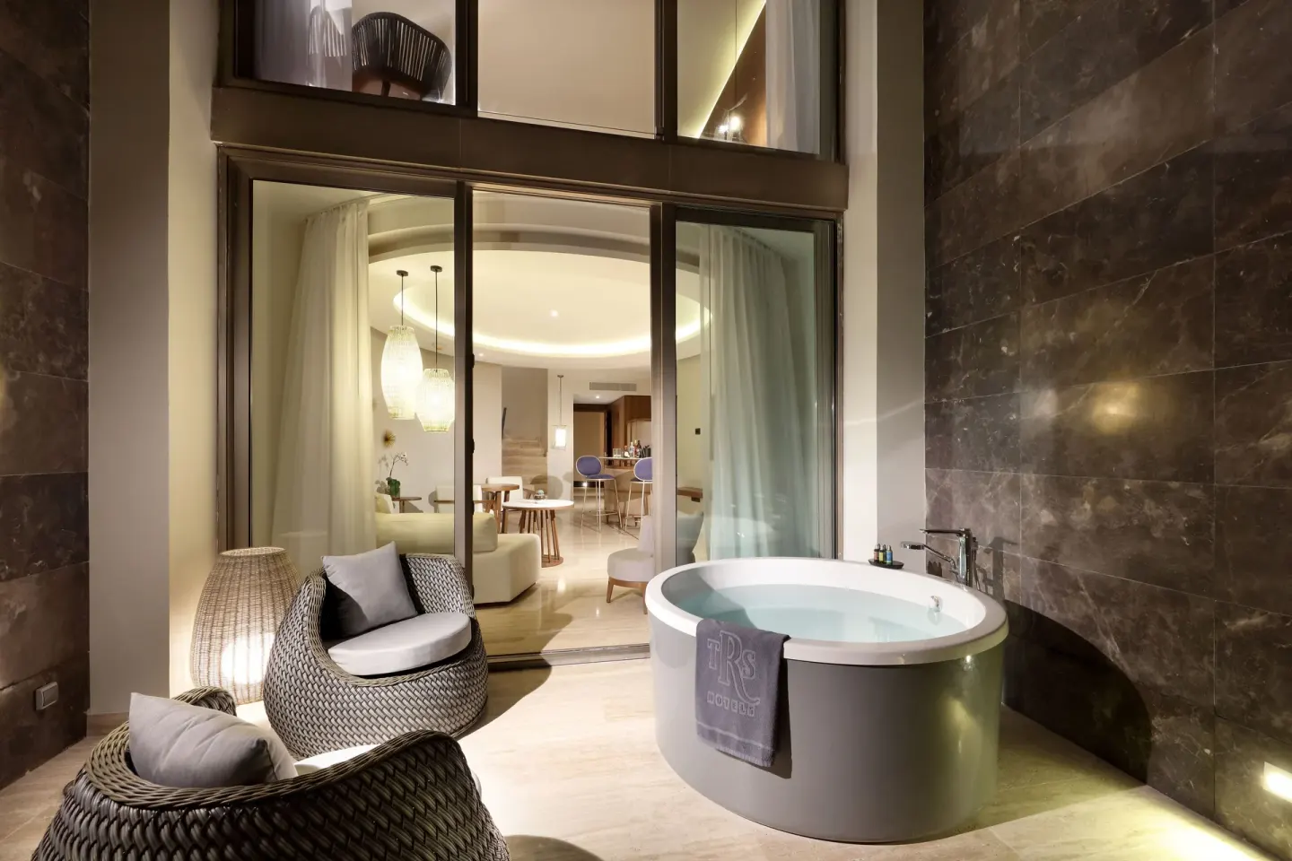 Loft Suite terrace at TRS Coral Hotel with Jacuzzi, woven chairs, and the living room beyond glass doors.