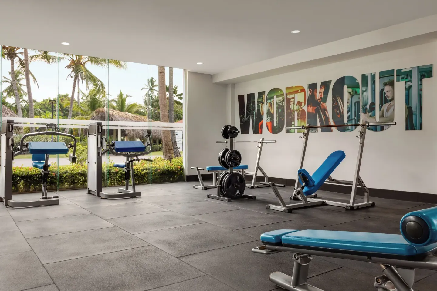 Weight room with blue benches and large windows at TRS Turquesa Hotel.