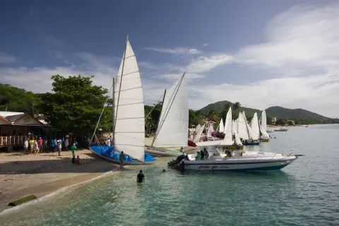 Sailboats line a sandy beach with people by the water near True Blue Bay Resort.
