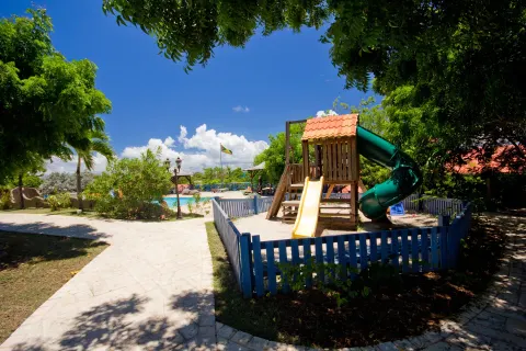 Fenced playground with slides beside a pool and garden paths at True Blue Bay Resort.