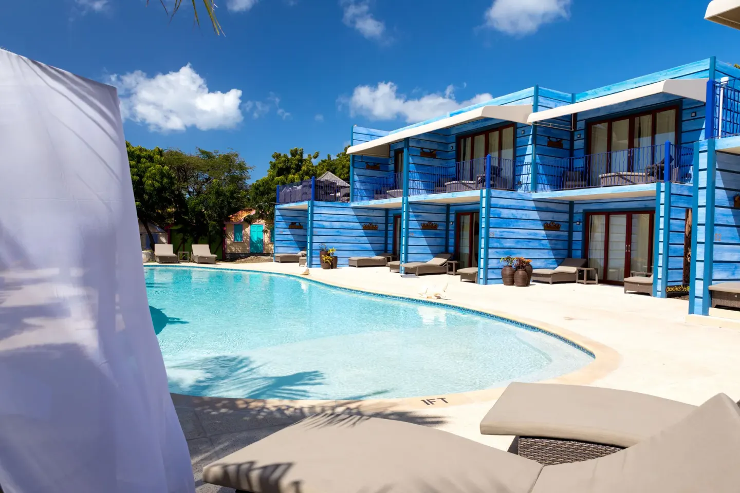 A pool curves beside bright blue guest buildings at True Blue Bay Resort.