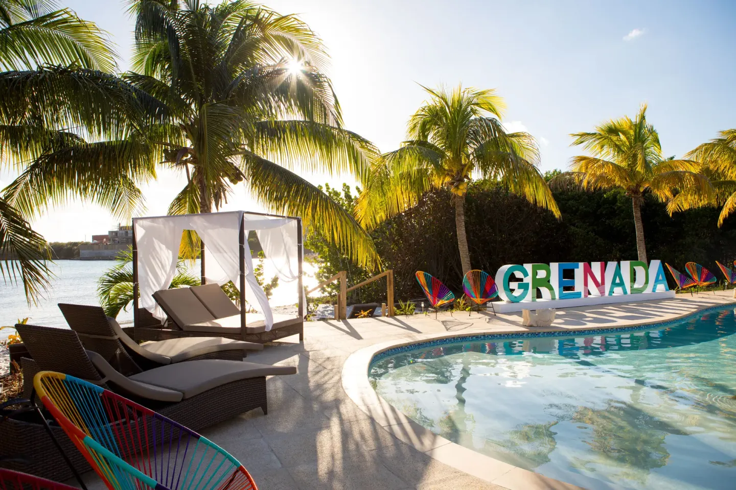 Poolside loungers, cabana, palms, and Grenada sign at True Blue Bay Resort.