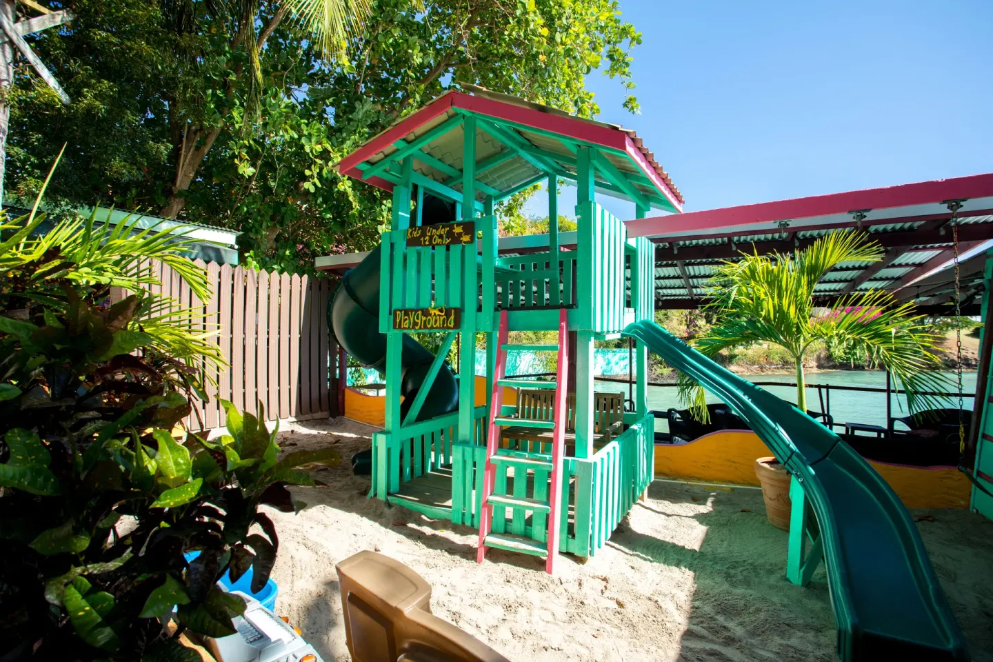 Sandy playground with green slides near the water at True Blue Bay Resort.