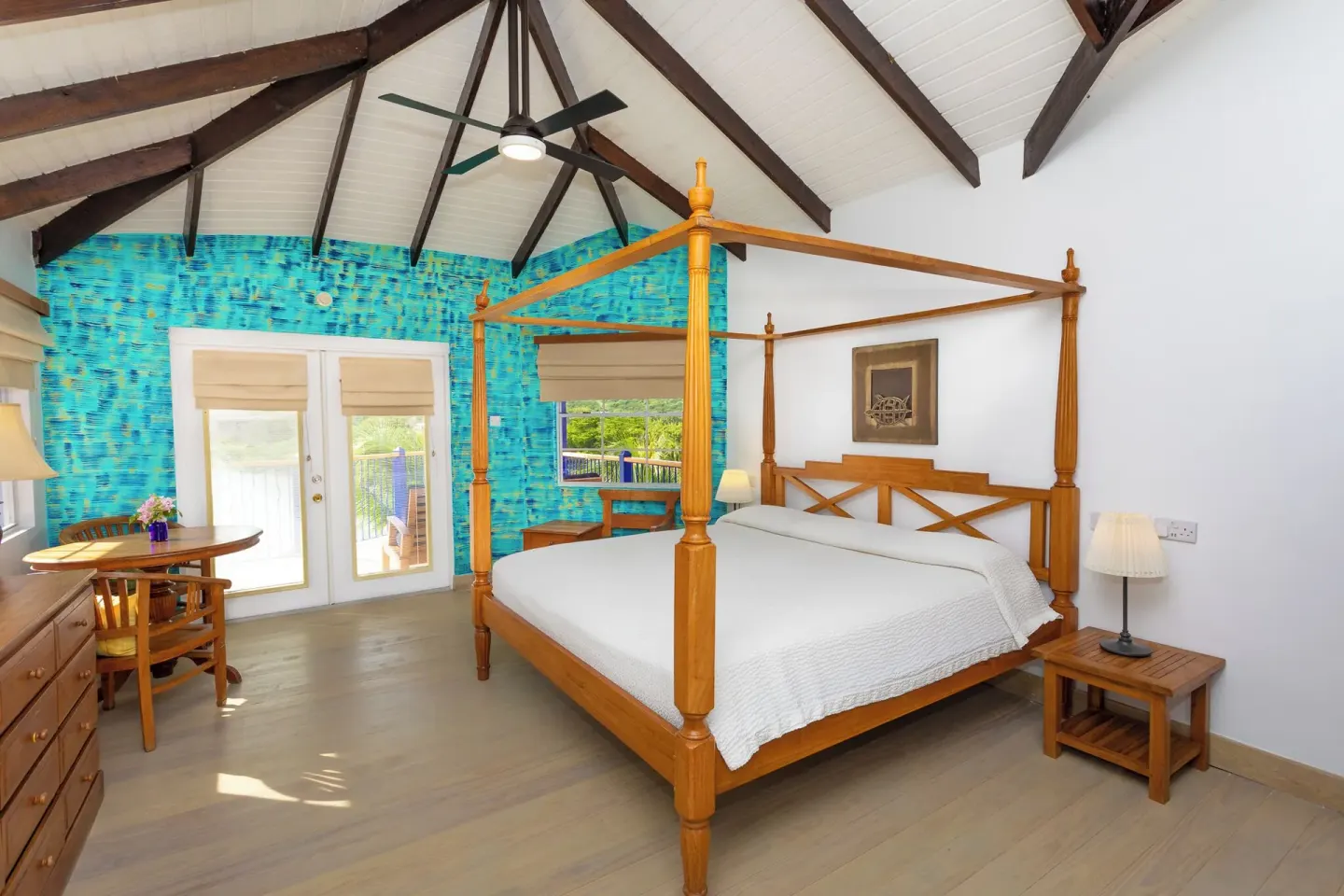 True Blue Bay Resort guest room with four-poster bed, vaulted ceiling, desk, and balcony doors.