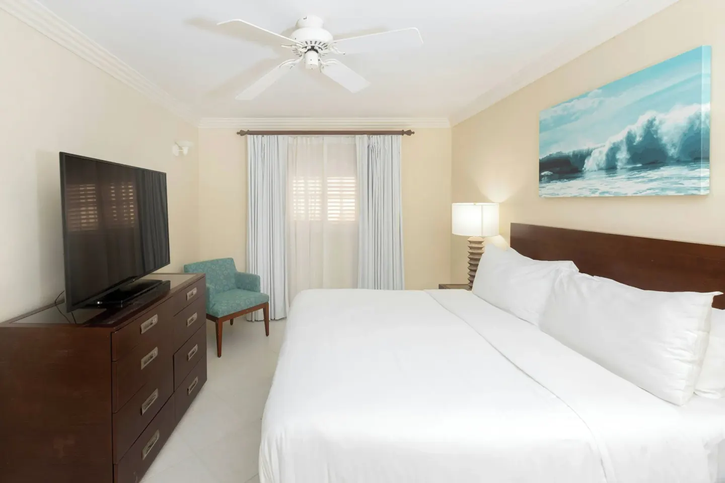 Guest room with white bed, dresser, TV, and wave artwork at Turtle Beach.