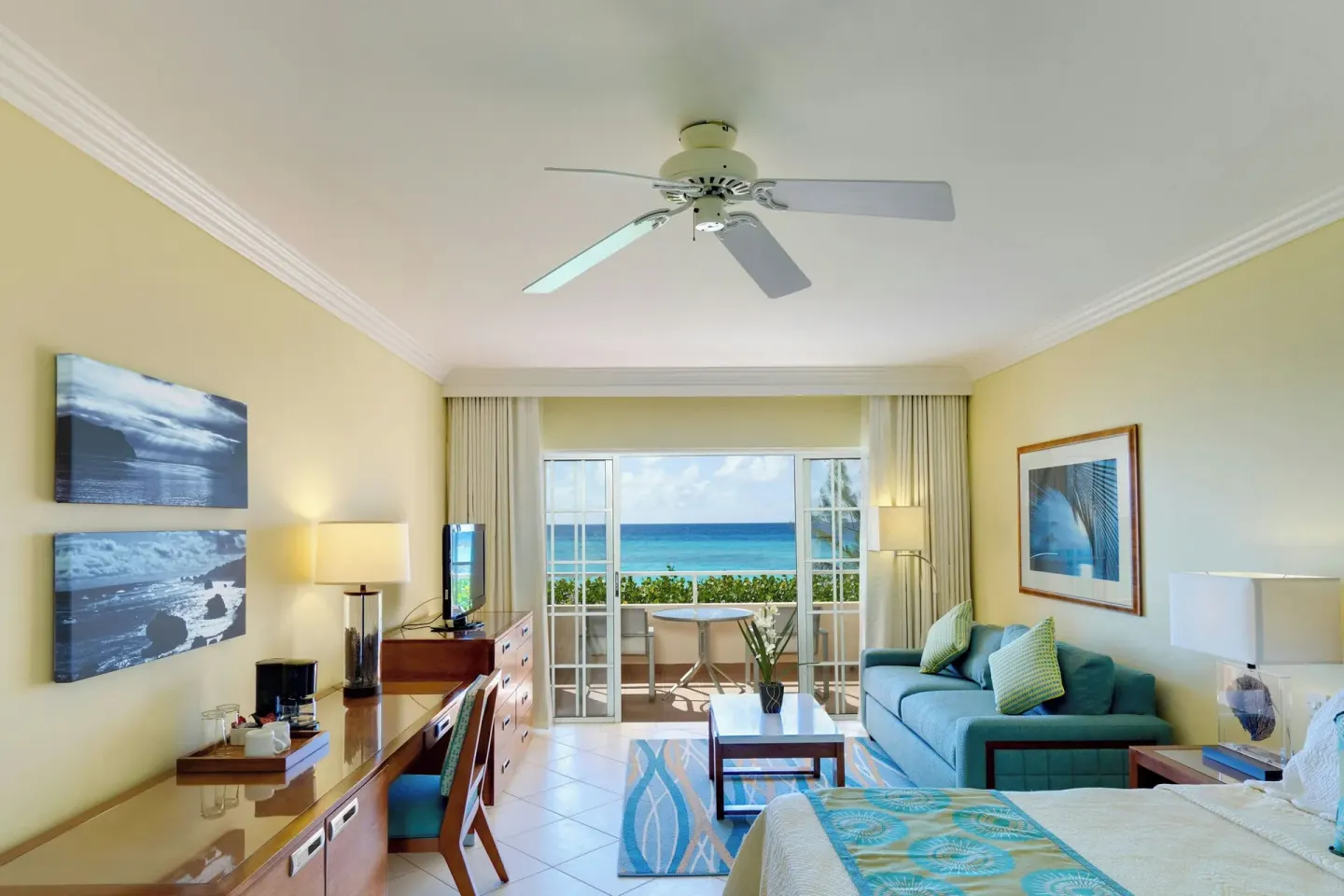 King bed guest room at Turtle Beach with desk, sofa and balcony view of the ocean.