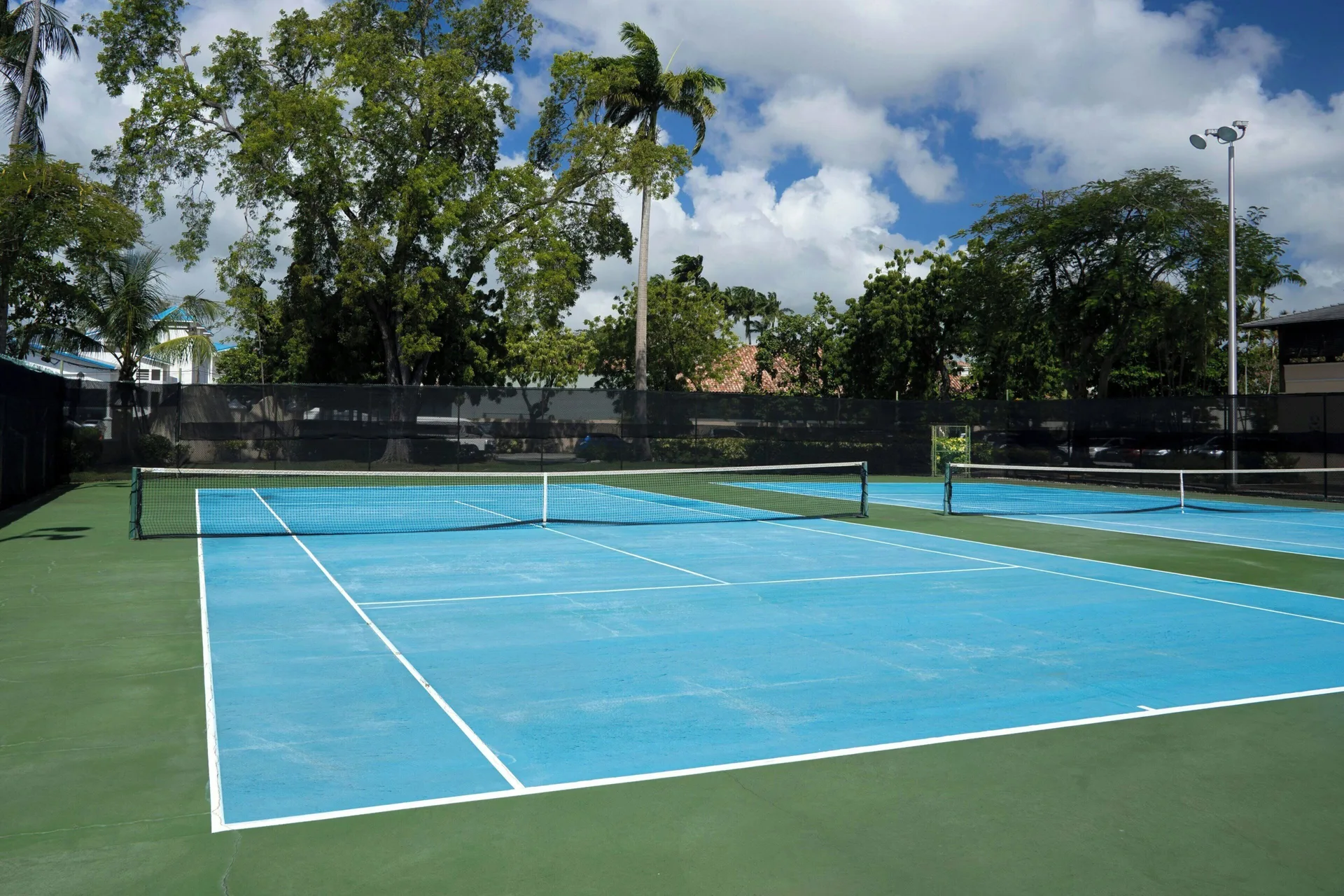 Outdoor tennis courts framed by tall trees and clouds at Turtle Beach.