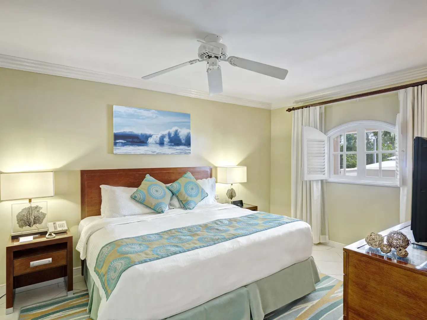 Junior suite bedroom at Turtle Beach with king bed, nightstands, arched window, and TV dresser.