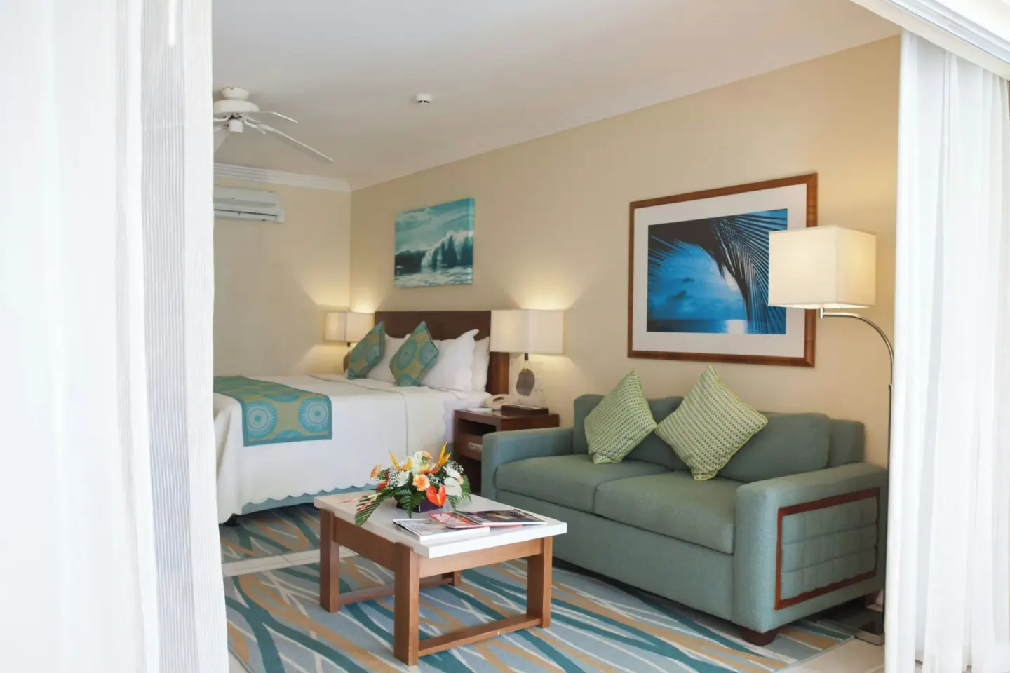 Junior suite at Turtle Beach with king bed, sofa bed, coffee table, lamps, and coastal artwork.