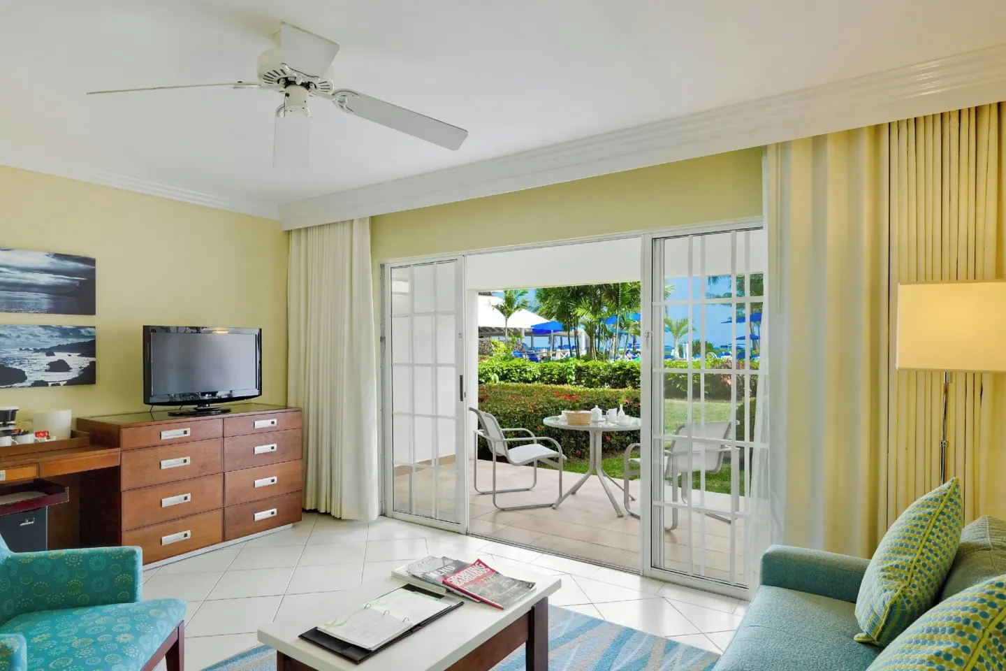 Junior suite living area at Turtle Beach with sofa, TV dresser, desk, and patio doors to gardens.