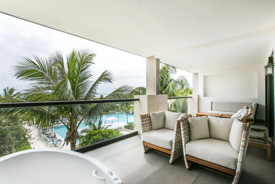 Balcony with cushioned chairs overlooking pool and palm trees at Unico Hotel Riviera Maya