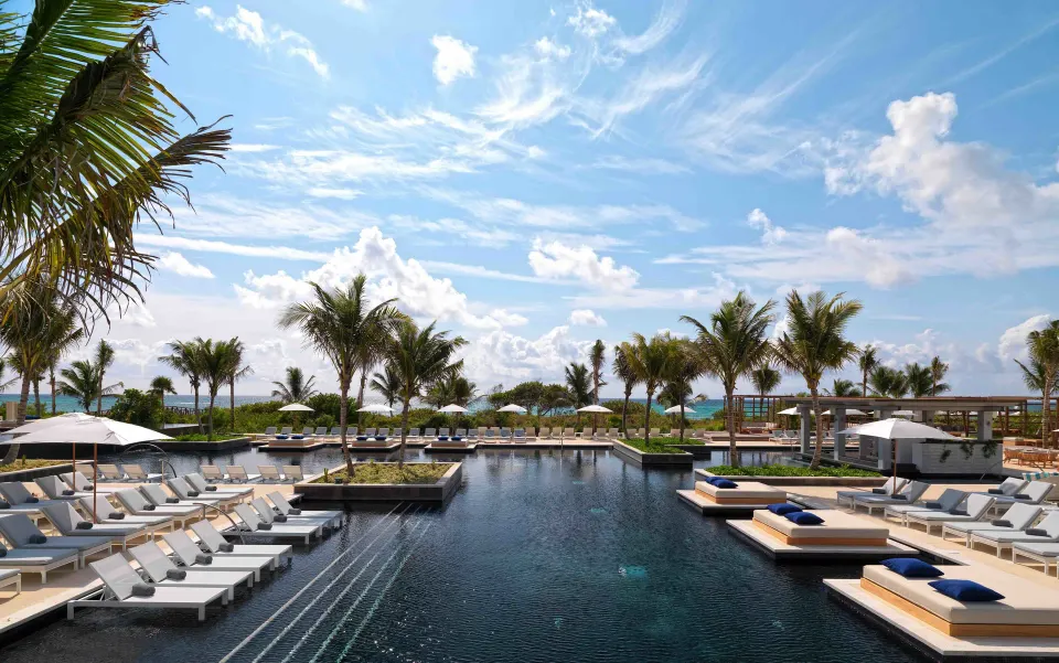 Resort infinity pool with loungers and palm trees at Unico Hotel Riviera Maya