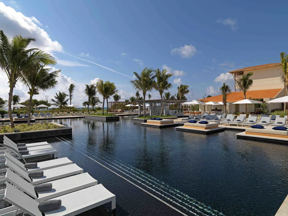 Side view of the resort pool with in-water loungers and palm trees at Unico Hotel Riviera Maya