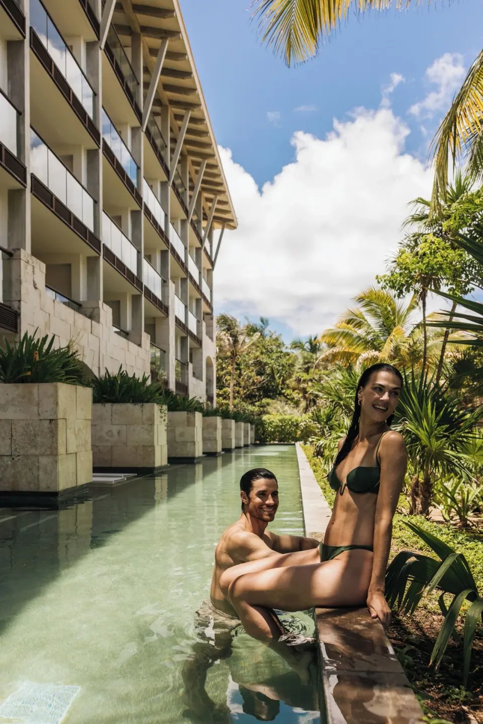 Guests sitting at a shallow pool next to the resort building at Unico Hotel Riviera Maya