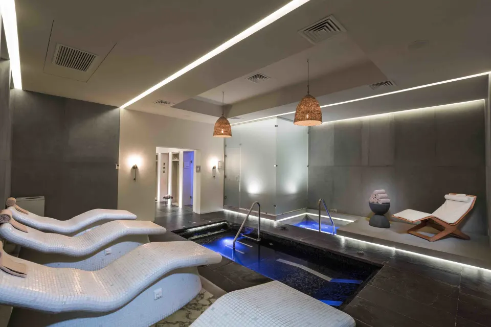 Indoor spa pool with illuminated water and lounge chairs at Unico Hotel Riviera Maya