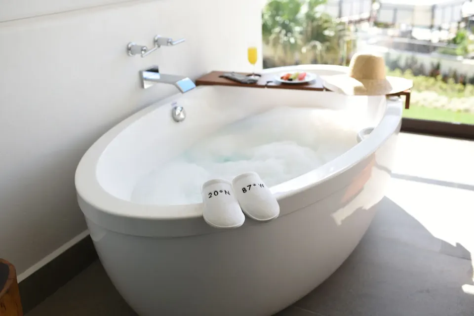 Freestanding bathtub with bubbly water and slippers on the rim at Unico Hotel Riviera Maya