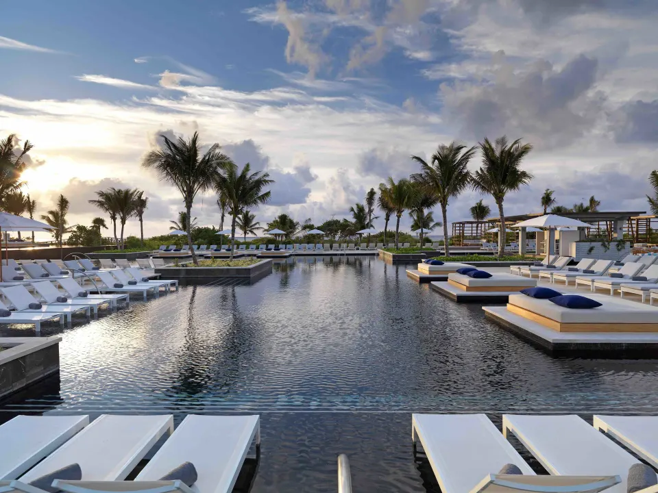 Resort pool at sunset with rows of white loungers and palm trees at Unico Hotel Riviera Maya