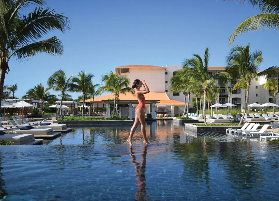 Woman walking across reflective infinity pool at Unico Hotel Riviera Maya
