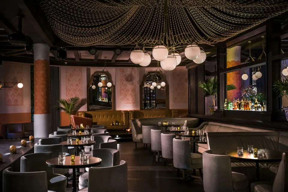 Dimly lit lounge bar with round tables and chandeliers at Unico Hotel Riviera Maya