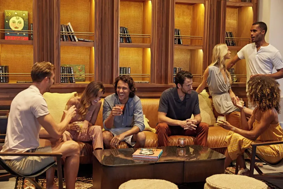 Group of friends laughing on leather sofas in a library-style lounge at Unico Hotel Riviera Maya