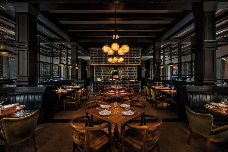 Wide view of a dimly lit dining room with round tables and booth seating at Unico Hotel Riviera Maya