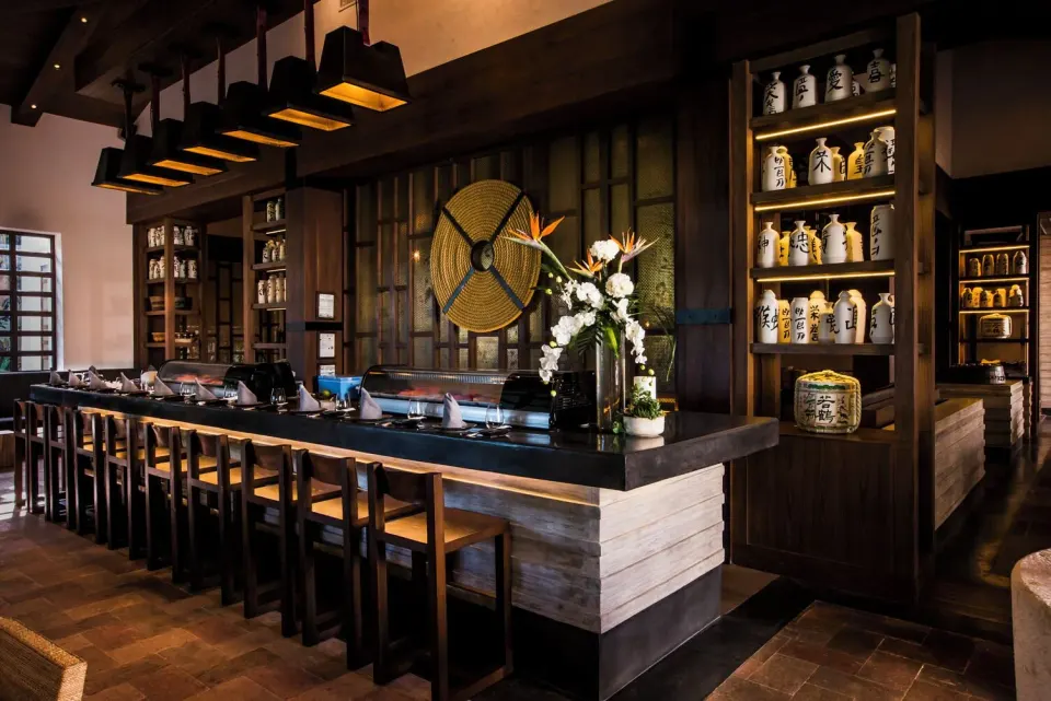 Long sushi counter with stools and shelves of ceramic jars at Unico Hotel Riviera Maya