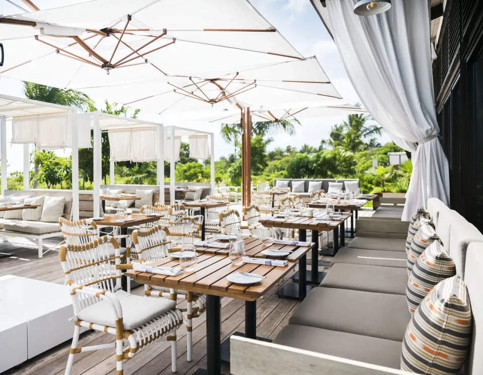 Sunlit terrace dining with umbrellas and cushioned benches at Unico Hotel Riviera Maya