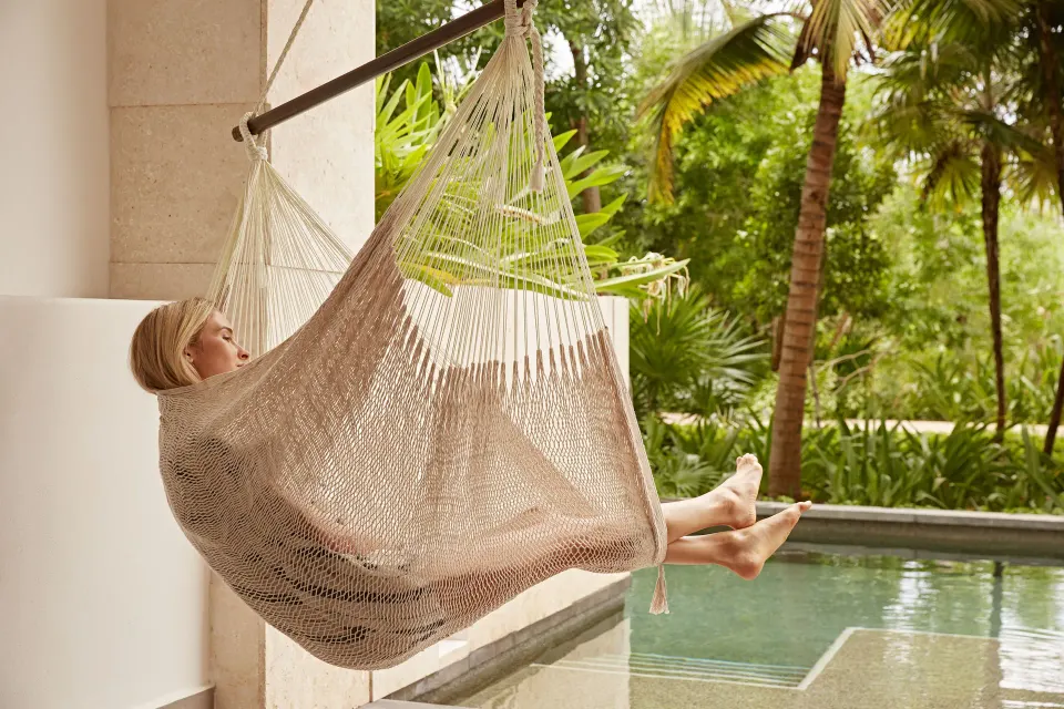 Guest reclining in hammock over Alcoba swim-up pool with tropical greenery at Unico Hotel Riviera Maya