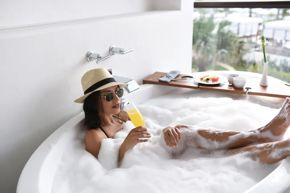 Guest relaxing in a bubble bath with a drink beside a window at Unico Hotel Riviera Maya