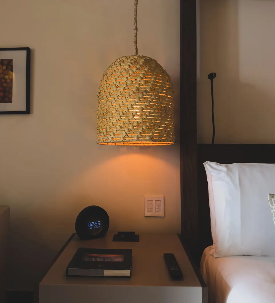 Bedside table with woven pendant lamp and alarm clock in Pure Wellness Alcoba at Unico Hotel Riviera Maya